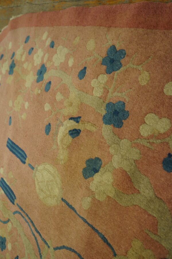 A low-pile pink rug displays a relief cut floral and branch pattern in pale yellow and deep blue.