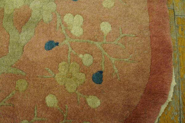 Dusty rose rug with green vines and blue berries rests on a peeling yellow wooden floor.