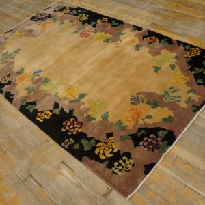 Tan rug with a black and brown stepped border decorated with multicolored floral motifs on wood flooring.