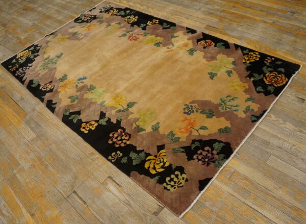 Tan rug with a black and brown stepped border decorated with multicolored floral motifs on wood flooring.