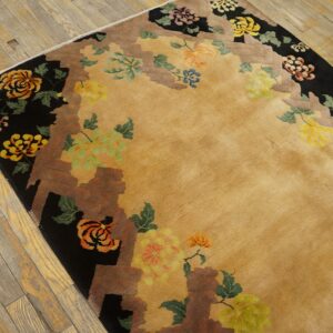 Tan rug with colorful floral motifs, black and brown stepped edges, lies on worn hardwood flooring.