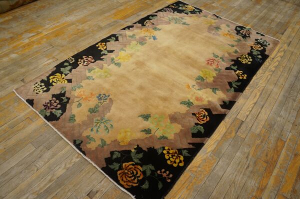 Rectangular rug with a light gold center and multicolor floral motifs along a black and brown stepped border.