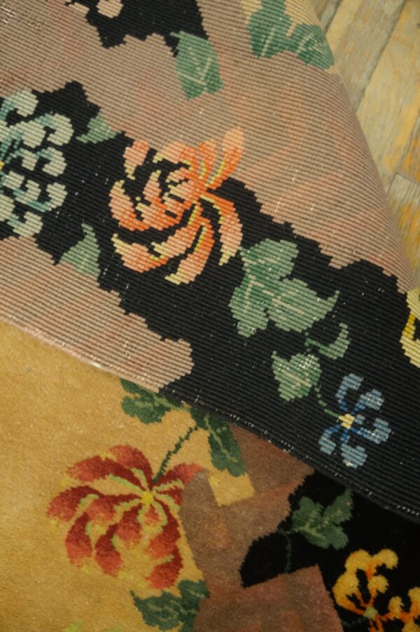 Detail of a rolled rug edge revealing tightly woven black and peach floral borders over a gold low-pile rug.