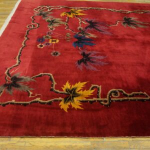 Deep red rug featuring a border of stylized multicolored leaves and winding dark vines on light wood flooring.