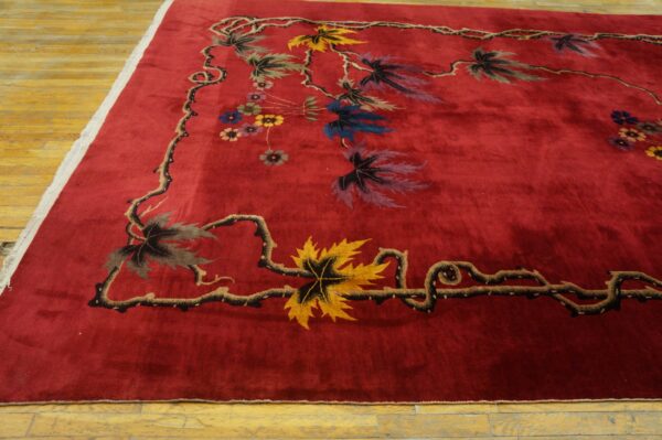 Deep red rug featuring a border of stylized multicolored leaves and winding dark vines on light wood flooring.
