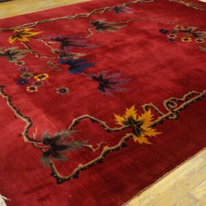 A deep red rug with a low pile featuring a thorny vine border with multicolored maple leaves and small flowers, displayed on wood floors.