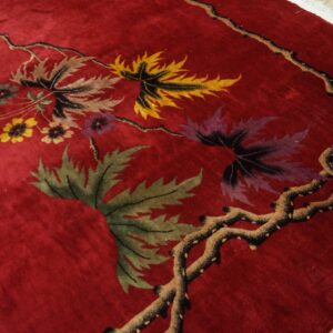 Deep red plush rug with multicolor botanical leaves and flowers visible near light wood flooring.