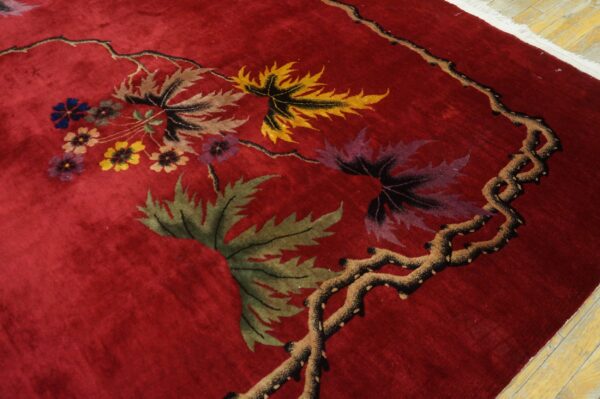 Deep red plush rug with multicolor botanical leaves and flowers visible near light wood flooring.