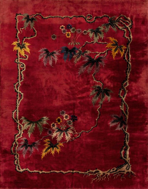 A deep red rug featuring a meandering vine border and colorful autumn leaves and small flowers.