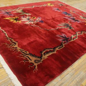 A plush, deep red rug with a multicolored botanical vine pattern lies on light wooden floorboards.
