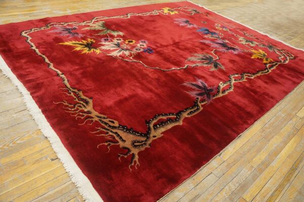 A plush, deep red rug with a multicolored botanical vine pattern lies on light wooden floorboards.