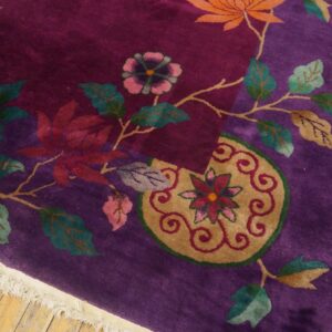 Deep purple rug displaying large floral and vine motifs in orange, teal, and gold on light wood flooring.