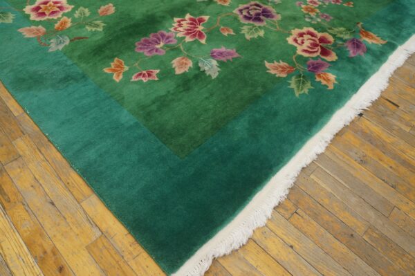 High-pile green rug featuring multi-colored floral designs and a teal border, resting on distressed wood planks.