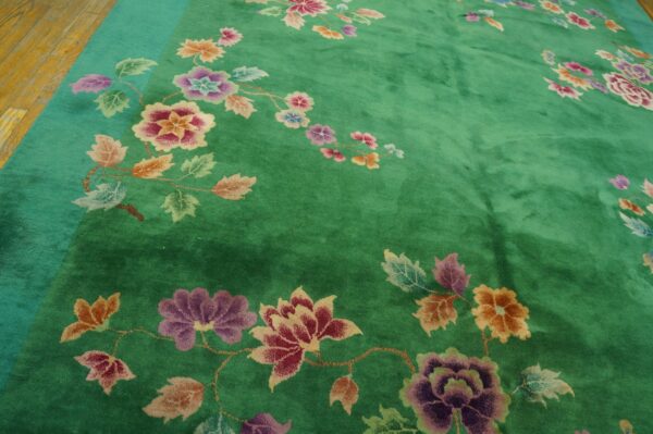 Deep green rug with large multicolored floral vines and a light teal border on wood flooring.