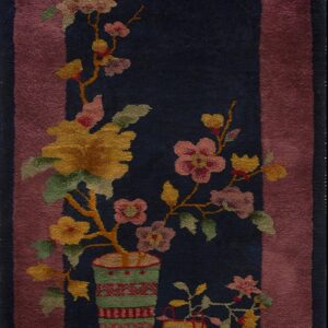 Dark blue low-pile rug featuring a central floral arrangement in patterned vases and a dusty rose border.