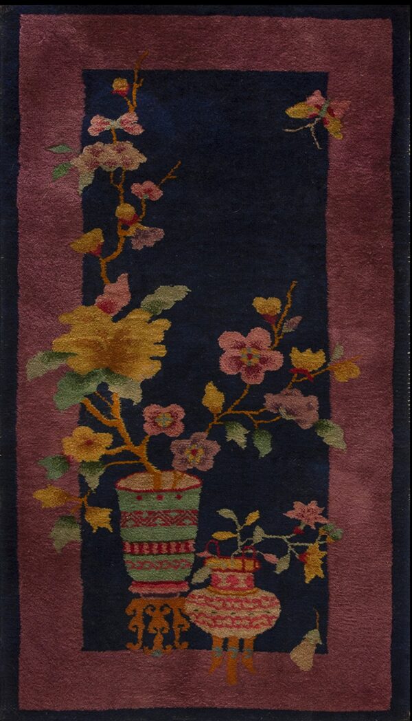 Dark blue low-pile rug featuring a central floral arrangement in patterned vases and a dusty rose border.