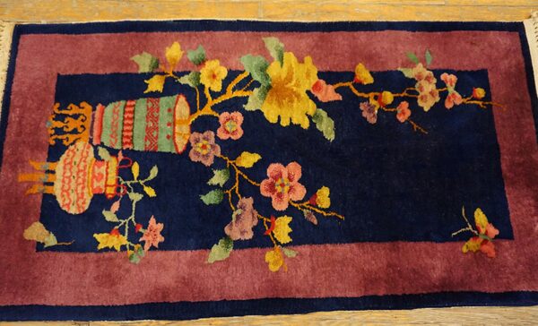 Navy rug with a wide mauve border featuring a central floral and vase design on light wood flooring.