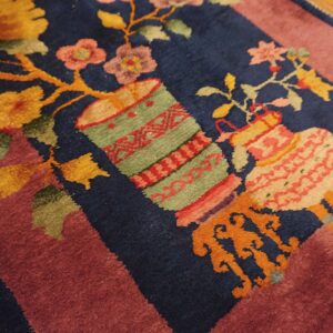 Navy blue rug detail with floral and vessel motifs bordered by mauve, resting on wood flooring.