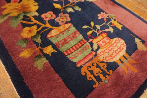 Navy blue rug detail with floral and vessel motifs bordered by mauve, resting on wood flooring.