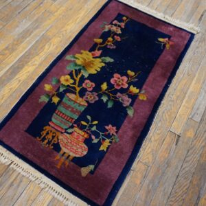 A small navy blue rug with a floral vase design and magenta border lies on aged wood floorboards.