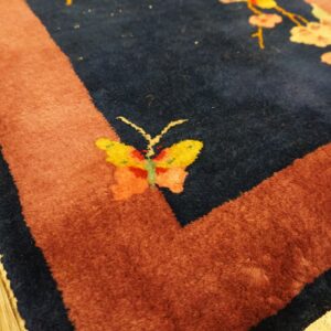 A deep blue rug with a rust border displays a yellow butterfly and pale pink flowering branches on wood flooring.