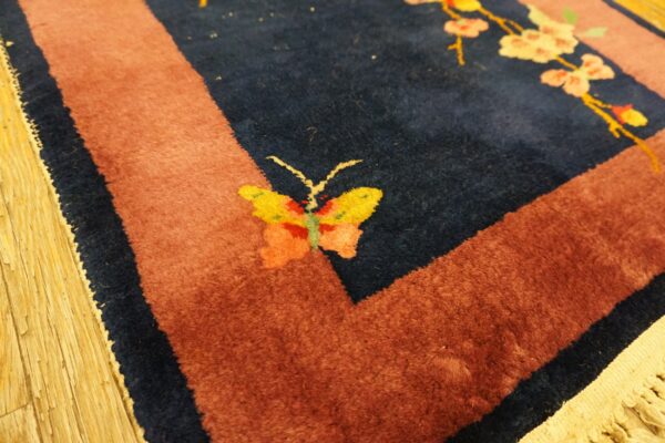 A deep blue rug with a rust border displays a yellow butterfly and pale pink flowering branches on wood flooring.