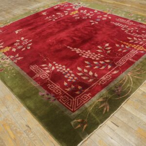 Red floral rug with a thick olive green border rests on worn light-colored wood planks.