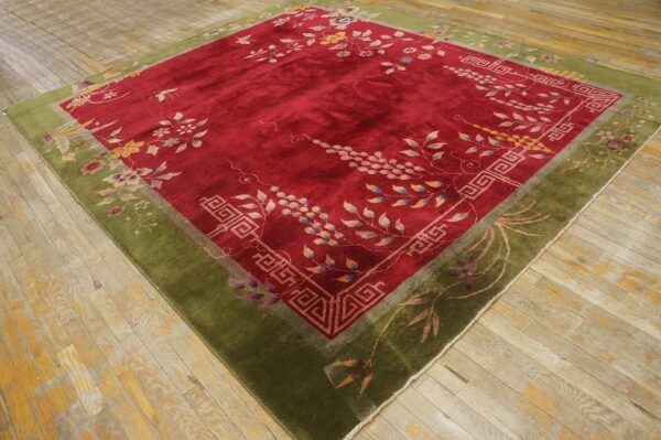 Red floral rug with a thick olive green border rests on worn light-colored wood planks.