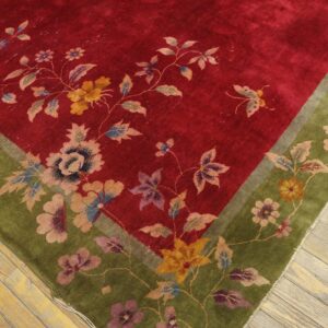 Close-up of a plush red and green floral rug resting on distressed light wood floorboards.