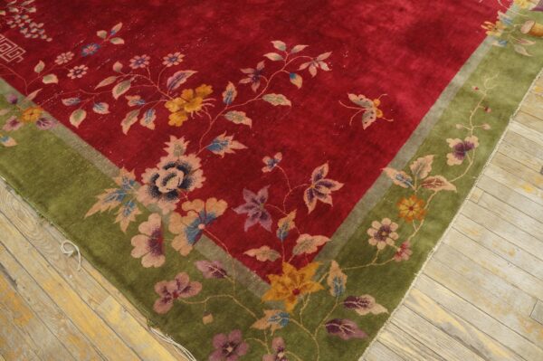 Close-up of a plush red and green floral rug resting on distressed light wood floorboards.