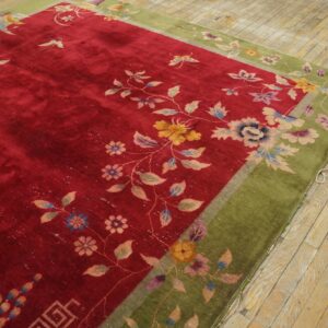 A velvety red floral rug with a moss green border rests diagonally on distressed wood flooring.