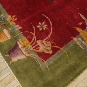 Floral patterned rug corner showing a deep red field and wide green border on light wood floors.