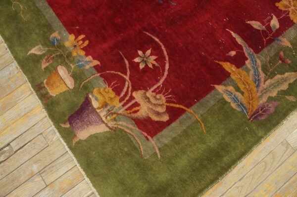 Floral patterned rug corner showing a deep red field and wide green border on light wood floors.