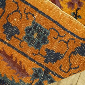 Textured orange and navy geometric rug edge folded over a high-pile floral section on light wood planks.