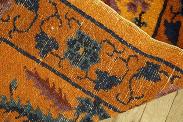 Textured orange and navy geometric rug edge folded over a high-pile floral section on light wood planks.