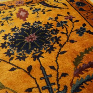 Close-up of a mustard yellow rug patterned with navy, teal, and maroon classical floral designs on wood floor.