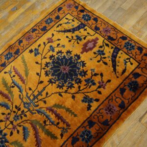 Gold rug with a navy and purple floral pattern and plush pile on distressed wood flooring.