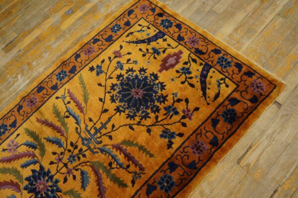 Gold rug with a navy and purple floral pattern and plush pile on distressed wood flooring.