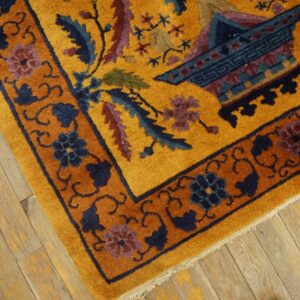 Golden yellow rug with complex blue and purple floral motifs and a rust border on wood plank flooring.