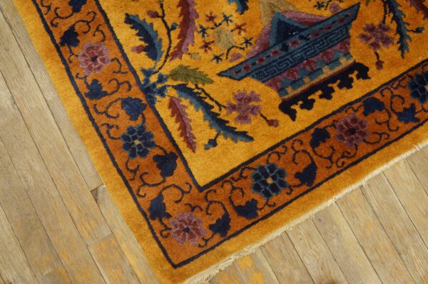 Golden yellow rug with complex blue and purple floral motifs and a rust border on wood plank flooring.