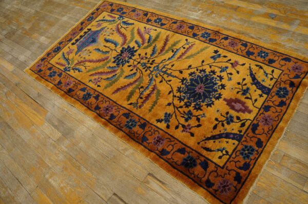A golden yellow rug with navy and maroon floral designs rests on weathered wooden floorboards.
