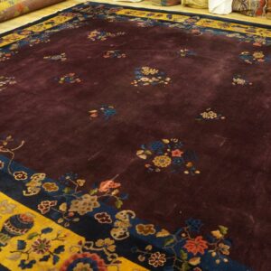 High-pile burgundy rug with scattered multicolored florals and a dramatic yellow and blue border on wood flooring.