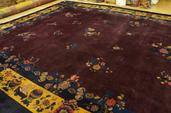High-pile burgundy rug with scattered multicolored florals and a dramatic yellow and blue border on wood flooring.