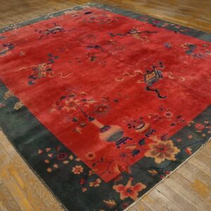 Red field rug with blue and yellow floral motifs, a wide dark green border, resting on worn wooden planks.