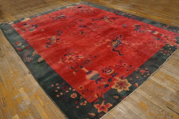Red field rug with blue and yellow floral motifs, a wide dark green border, resting on worn wooden planks.