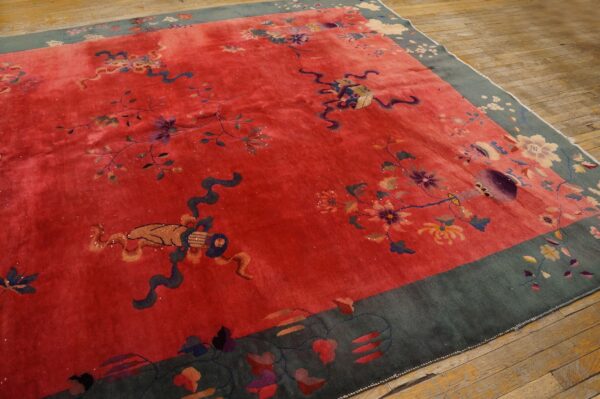Vivid red plush rug with scattered floral and ribbon motifs, framed by a dark blue-green patterned border on wood floors.