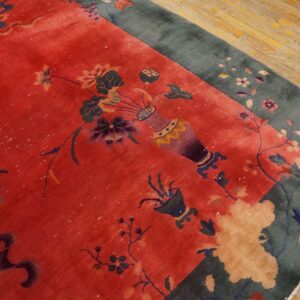 Plush red rug with vase and floral pattern, teal border, visible on aged light brown wood floor.