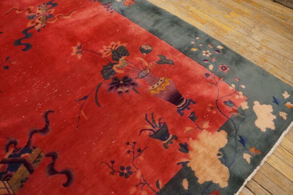 Plush red rug with vase and floral pattern, teal border, visible on aged light brown wood floor.