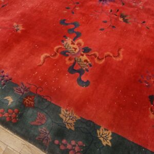 Red rug with stylized flowers and a dark teal border displaying leaves and berries over wood floor.