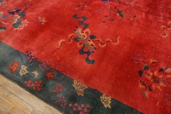 Red rug with stylized flowers and a dark teal border displaying leaves and berries over wood floor.
